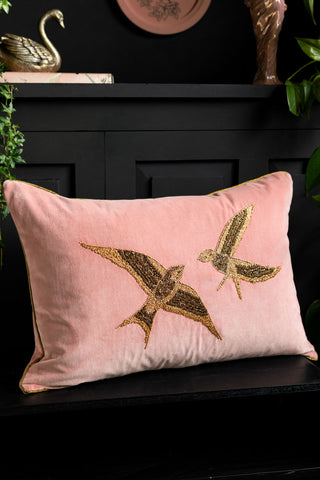 Love Birds Embroidered Pink Velvet Cushion against a black background, styled on a black bench 