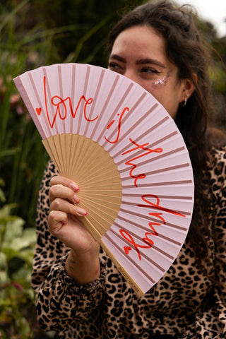 The Love Is The Drug Pink & Red Fan being held by a model outdoors.
