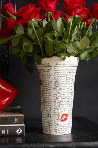 The Love Letters Flower Vase shown against a black wall with red roses and books. 