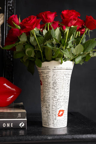 The Love Letters Flower Vase filled with red roses and displayed on a black sideboard against black walls. 