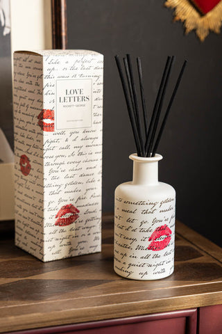 The Love Letters Reed Diffuser shown with the box in the background on a wooden console table against dark grey walls. 