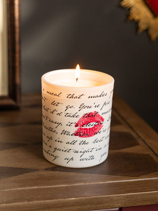 The Love Letters Scented Candle shown lit against dark walls on a wooden console table. 