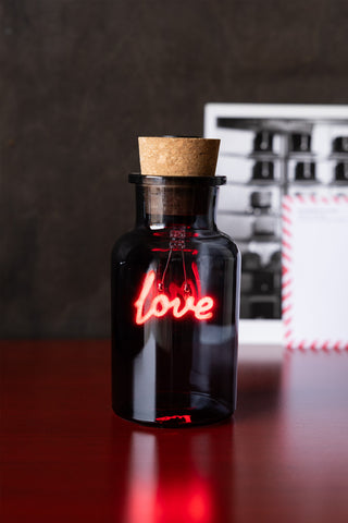 The Love Neon Bottle Light displayed on a wooden surface.