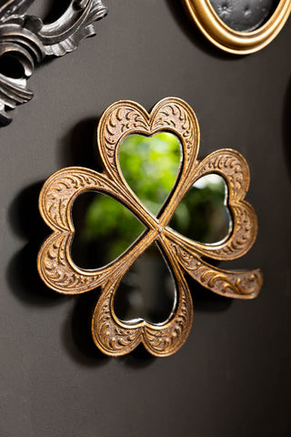 Lucky Clover Small Gold Wall Mirror shown on a black wall amongst black and gold art. 