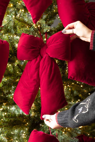 Lifestyle image of the Luxurious Red Velvet Cushion Bow Christmas Decoration - Small - held in hands on a tree