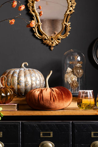 The Medium Rust Velvet Pumpkin shown on an apothecary-style sideboard with other pumpkins and a gold mirror on the wall. 
