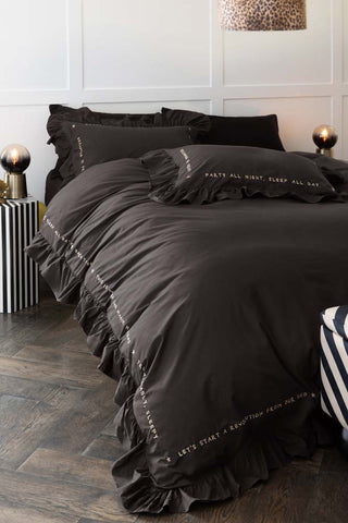 Lifestyle image of the Charcoal Grey Mega Frill Duvet Cover and Pillowcase Set styled on a bed in front of a panelled wall with various home acessories. 