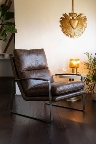 The Minimalist Brown Leather Lounge Chair styled next to a side table and lamp, with some plants in the bckground.