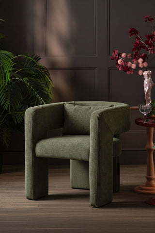 The Modern Green Accent Chair with Bolster Cushion styled next to a side table with accessories on, with a plant in the background.