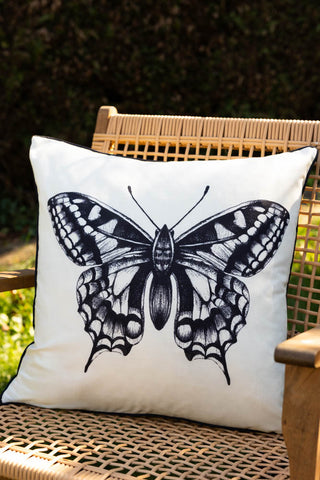 The Monochrome Butterfly Outdoor Cushion styled on a woven chair outdoors.