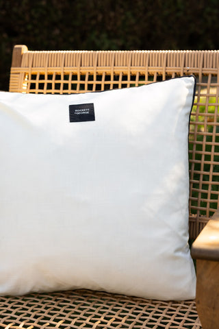 The reverse side of the Monochrome Butterfly Outdoor Cushion, displayed on a wicker chair outdoors.