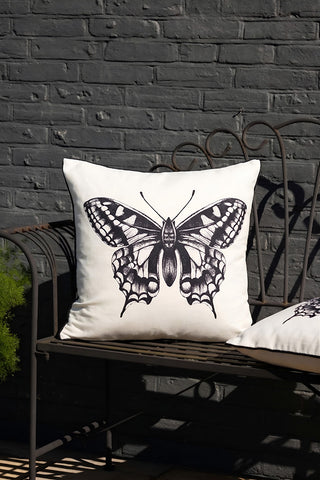 Two of the Monochrome Butterfly Outdoor Cushions, styled on a garden bench next to a plant.