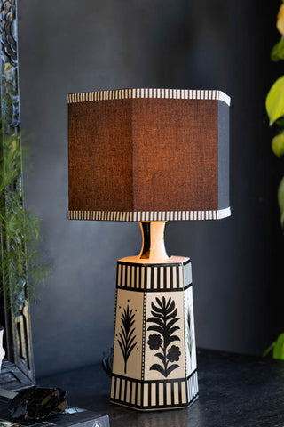 The Monochrome Folklore Floral Table Lamp shown with the light on against a black wall. 