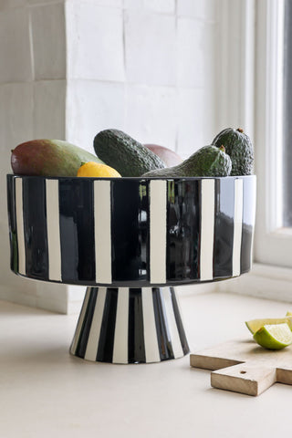Lifestyle image of the Black & White Stripe Bowl styled with fruit inside next to a chopping board by a window. 