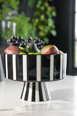 Lifestyle image of the Black & White Stripe Bowl displayed on a white table with fruit inside. 