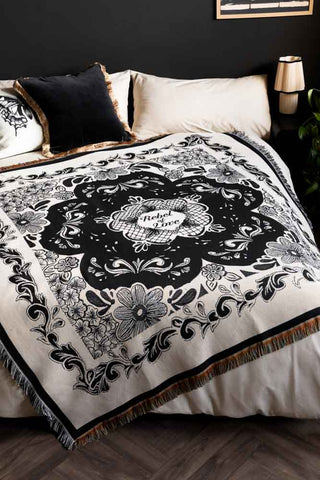 The Monochrome Forever Rebel Woven Throw shown against plain off-white bedding and black walls. 