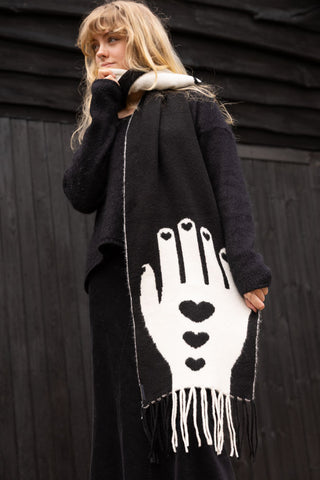 A full-length shot of a model wearing a black and white scarf that features a white hand with black hearts motifs 