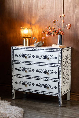 The Monochrome Rose Noir Chest Of Drawers with a lamp and various accessories on, in front of a dark wall.