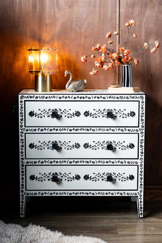 The Monochrome Rose Noir Chest Of Drawers in front of a dark wall styled with various accessories on.