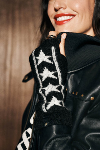 The Monochrome Stars Handwarmers shown worn against a leather jacket on a woman with red lipstick on. The design shows a black handwarmer with a border of white stars running down the length of the design. 