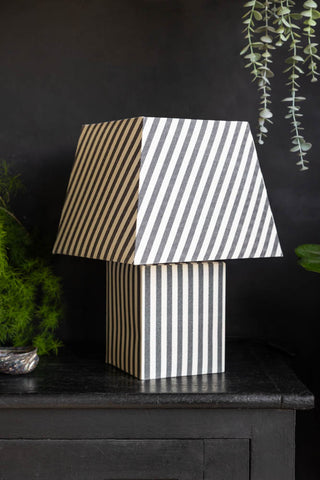 The Monochrome Stripe Table Lamp on a blacksideboard with some greenery.