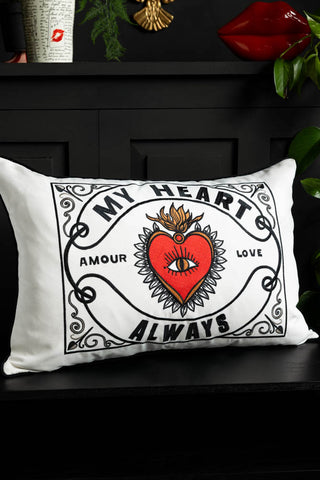 The My Heart Monochrome Embroidered Cushion shown on a black bench with red lips accessories on the shelf above. 