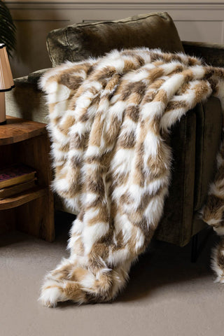 The Natural Abstract Faux Fur Throw show draped over a green velvet armchair with a wooden side table next to it. 