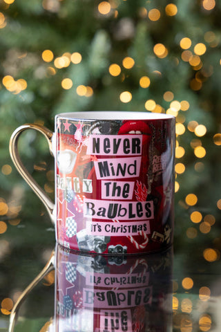 The Never Mind The Baubles Mug displayed on a dark mirrored surface with twinkling lights in the background.