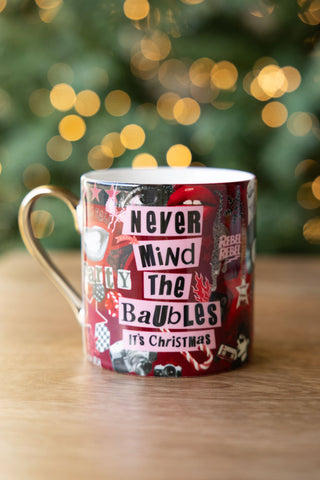 The Never Mind The Baubles Mug displayed on a wooden surface with twinkling lights in the background.