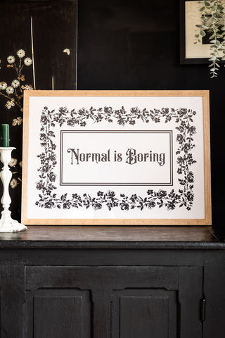 Styled shot of natural framed print with 'Normal is Boring' text on a dark background