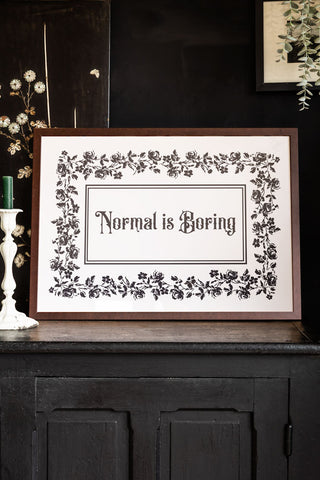 Styled shot of walnut framed print with 'Normal is Boring' text on a dark background