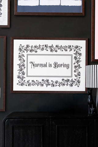 Framed print with 'Normal is Boring' text on a dark wall.