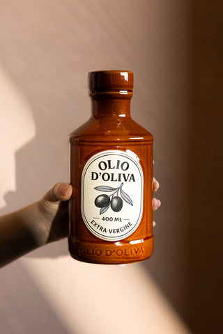 The Olio d'Olivia Ceramic Bottle Vase shown against a neutral wall with a hand holding the vase. 