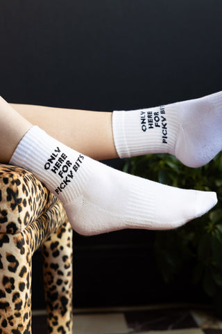 The Picky Bits White Socks shown on a model leant on a leopard print stool against a dark black wall. 