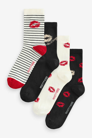The pack of 4 lips printed socks shown flat against a white background, one design shows tripe socks with red toe and heel sections and a kiss mark at the top of the sock, another shows a black sock with a beige kiss mark, the next shows a cream sock with red kiss marks all over the design and the final sock in the set is black with red and a cream kiss mark. 