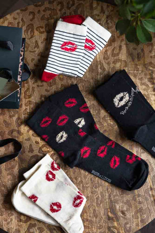 The Pack Of 4 Lips Printed Socks  displayed on a leopard print table with a gift bag and plant.