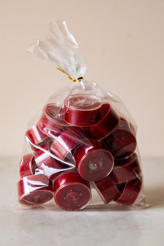 The Pack of 20 Tealight Candles in Deep Red in the bag, displayed on a white surface.