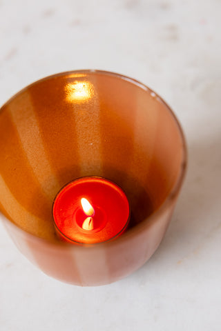 One of the Pack of 20 Tealight Candles in Deep Red lit and displayed inside a tealight holder.