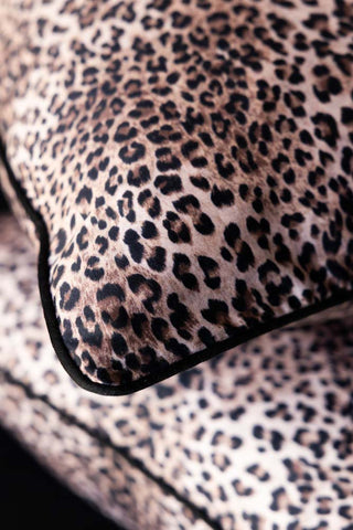 Close-up of a leopard print pillow with a piped black edge.