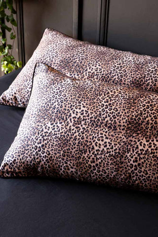 Leopard print pillowcases on a dark sheet in front of a panelled wall with some greenery.