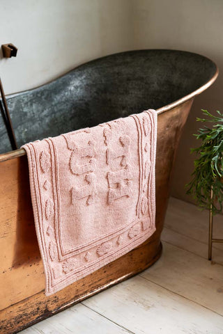 Bath Slut Blush Pink Bath Mat shown hanging over the side of a copper bath. 