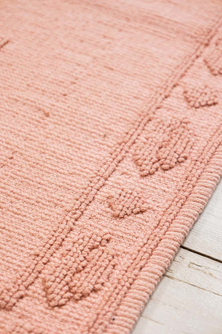 Close-up of a textured pink bath mat on a light wooden floor.