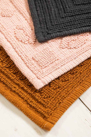 Three textured bath mats in pink, black, and brown on a white surface.
