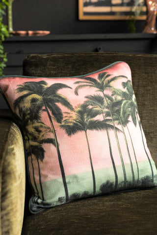 image of Palm Paradise Cushion with Piped Edge styled on a dark green sofa. 