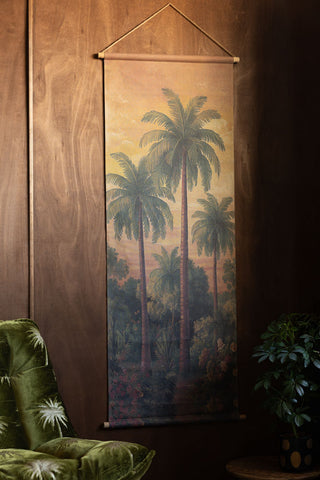 The Palm Tree Canvas Wall Hanging styled on a dark wall above a chair and plant.