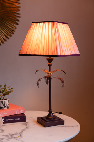 Styled image of the Palm Tree Table Lamp - Pink & Burgundy, switched on and on a white marble table