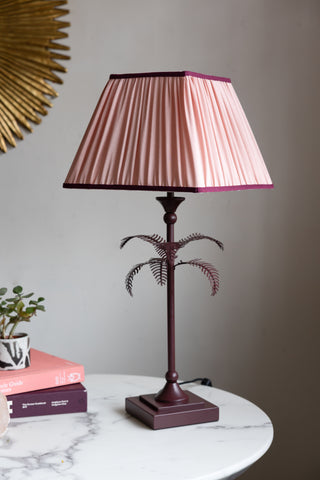 Styled image of the Palm Tree Table Lamp - Pink & Burgundy, switched off and on a white marble table