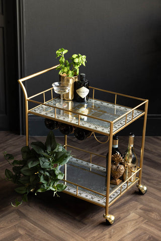 The Party People Only Gold Drinks Trolley, decorated with plants and drinks bottles on a dark background. 