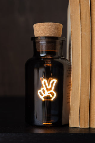 The Peace Neon Bottle Light displayed next to some books.