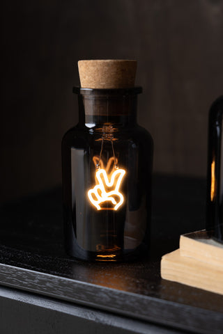 The Peace Neon Bottle Light on a dark wooden surface with some books and another bottle.